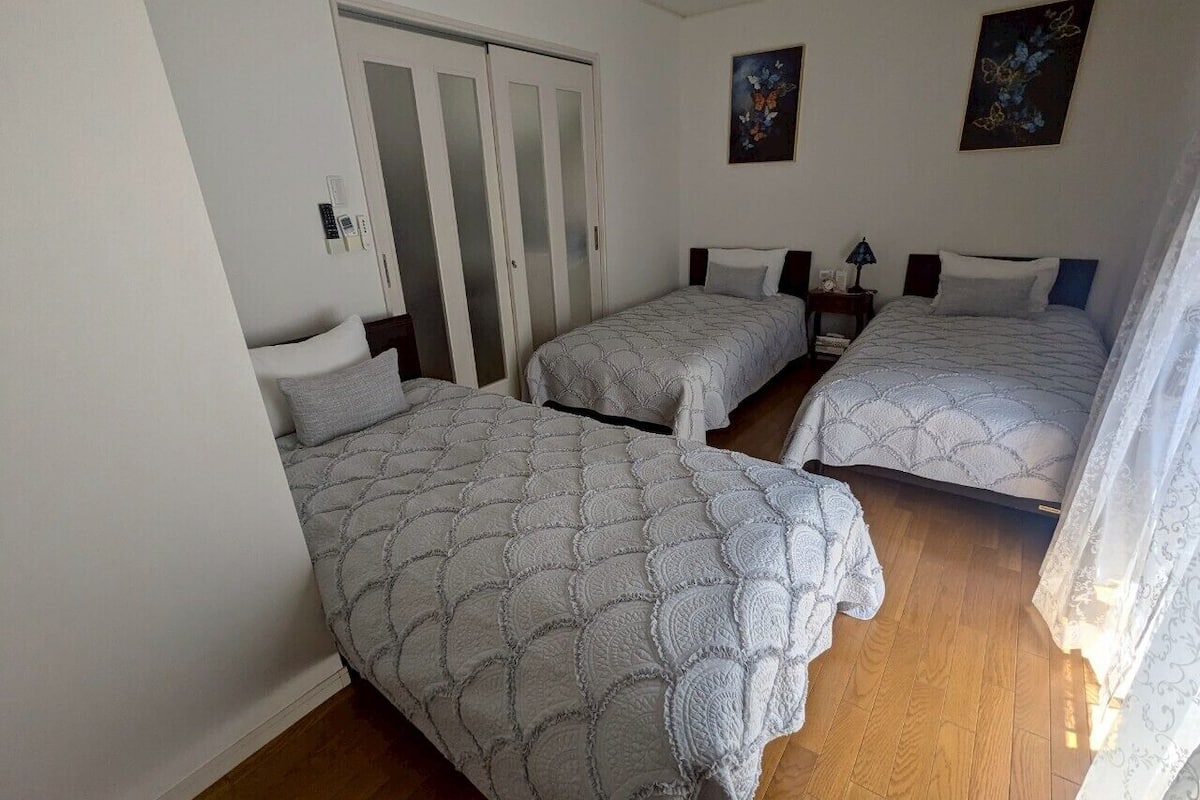 A room with three beds, a wardrobe, and a nightstand with a lamp.