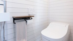 Un baño moderno con paredes de azulejos blancos, un inodoro, un perchero y un panel de control.