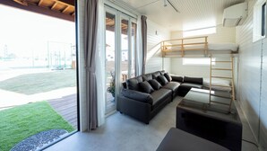 Una sala moderna con un sofá modular, una litera y un amplio ventanal corredera que da a un espacio exterior.