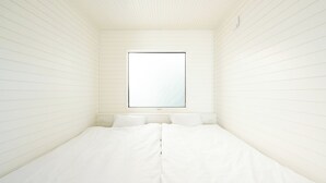 Una habitación pequeña, con una cama individual, ventana y paredes blancas.