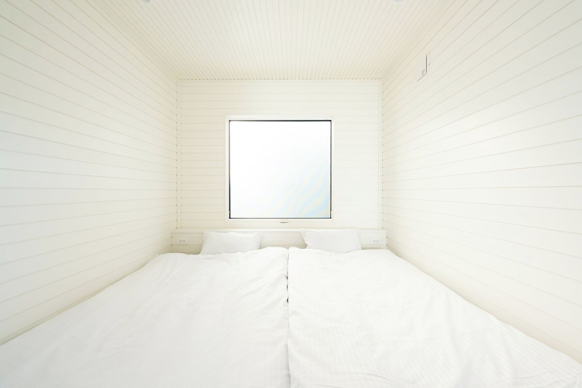Una habitación pequeña, con una cama individual, ventana y paredes blancas.