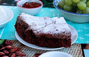 A slice of chocolate cake on a plate with a dusting of powdered sugar, accompanied by a bowl of grapes and a bowl of jam. - Le Torrette Etrusche 5 Room – Comfort and Relaxation in Capalbio (Capalbio)