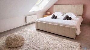 Une chambre avec un plafond en pente, un grand lit, une table de chevet, une lampe et un radiateur.