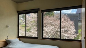 Un dormitorio con dos camas, una ventana con vistas a flores de cerezo y un taburete de madera.
