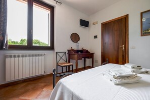 Ein Schlafzimmer mit Bett, Schreibtisch, Stuhl, Heizkörper, Fernseher und einer Tür.