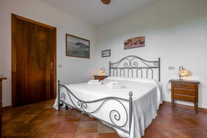 A bedroom with a bed, a wooden door, a nightstand, a lamp, and a wall with framed pictures. - Le Torrette Etrusche Room 6 – Comfort and Relaxation in Capalbio (Capalbio)