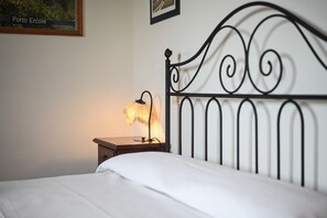 Een bed met een wit laken, een nachtkastje met een lamp en een wand met een ingelijst schilderij.