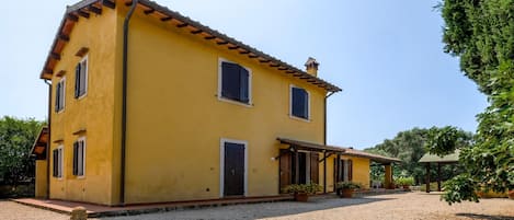 A two-story yellow building with a tiled roof, a gravel driveway, and a covered porch area.
