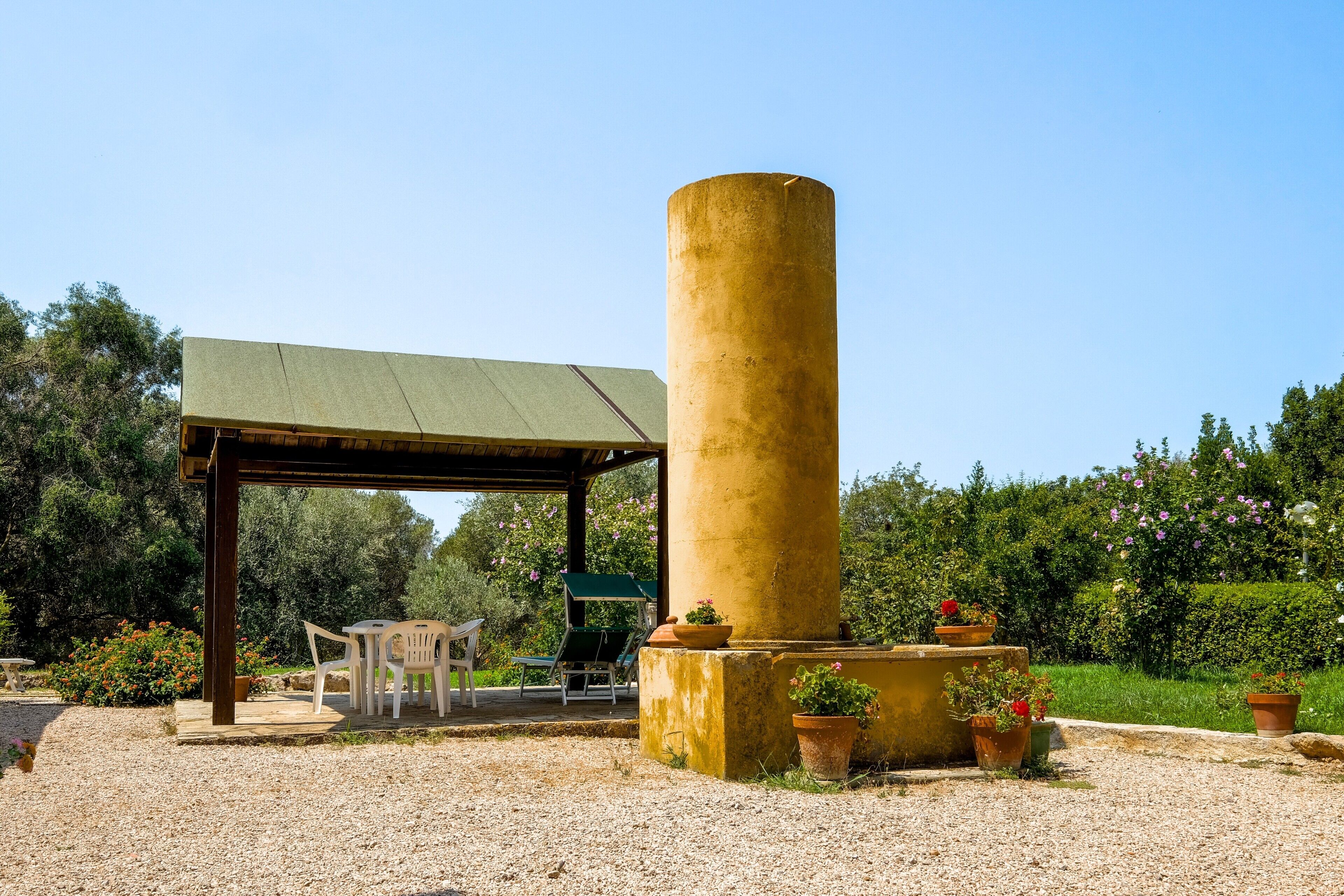 A covered outdoor seating area with a pergola, a cylindrical column, and potted plants.