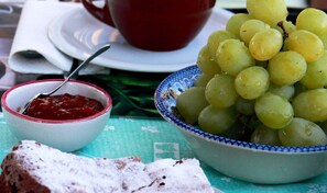 A table with a bowl of green grapes, a bowl of red jam, and a piece of bread. - Le Torrette Etrusche Room 6 – Comfort and Relaxation in Capalbio (Capalbio)