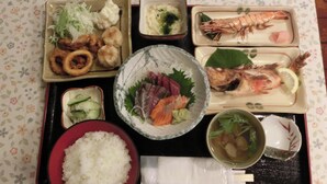 Un plateau contenant divers plats japonais, notamment du riz, du sashimi et des fruits de mer.