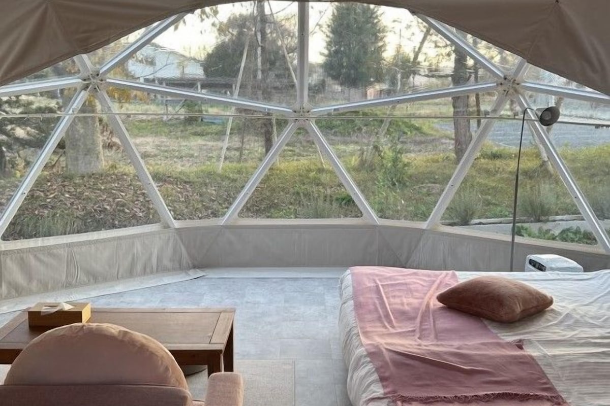 A tented accommodation with a bed, a table, and a chair.