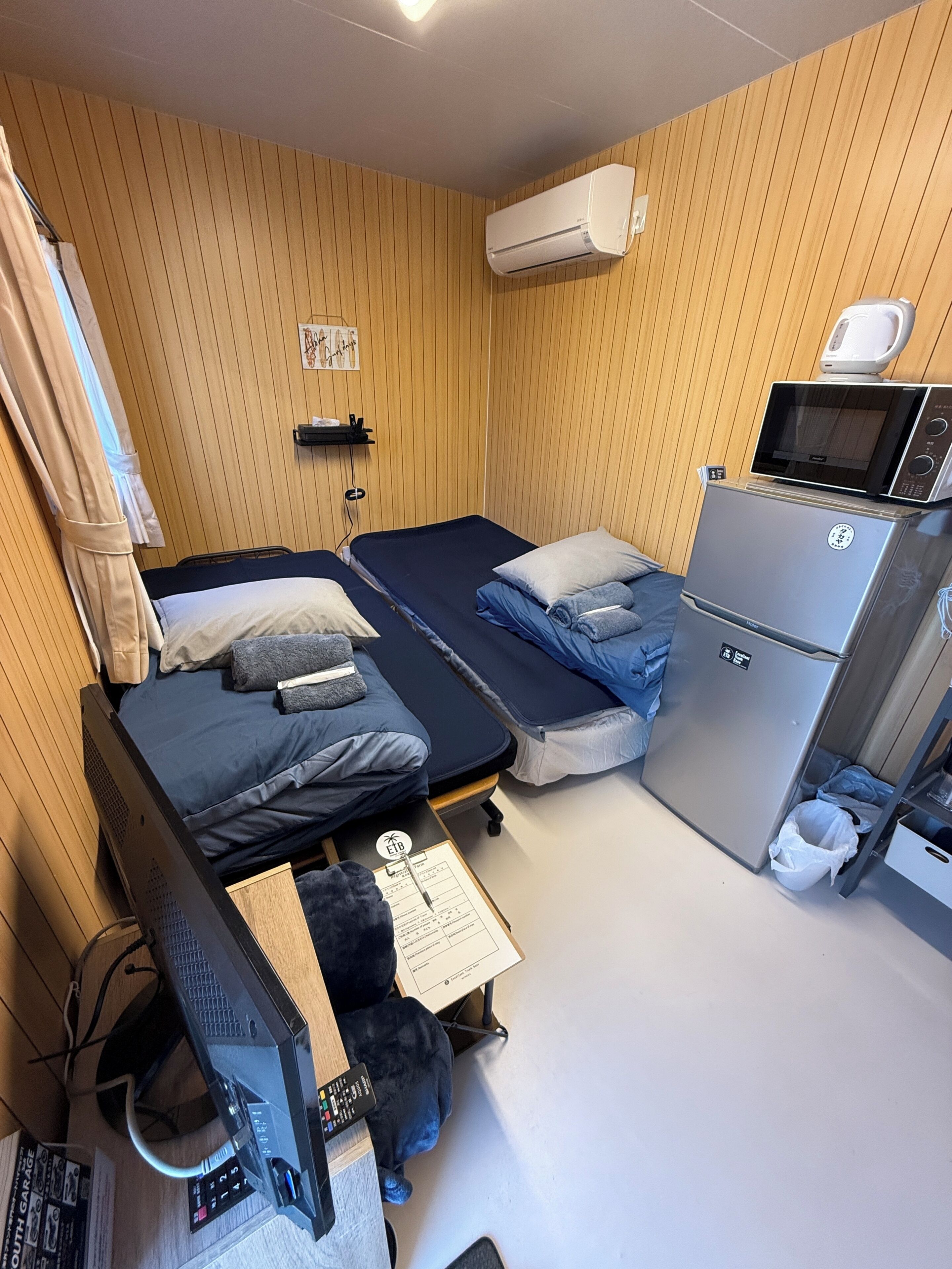 A compact room with two beds, a small kitchenette, a microwave, and a computer setup.