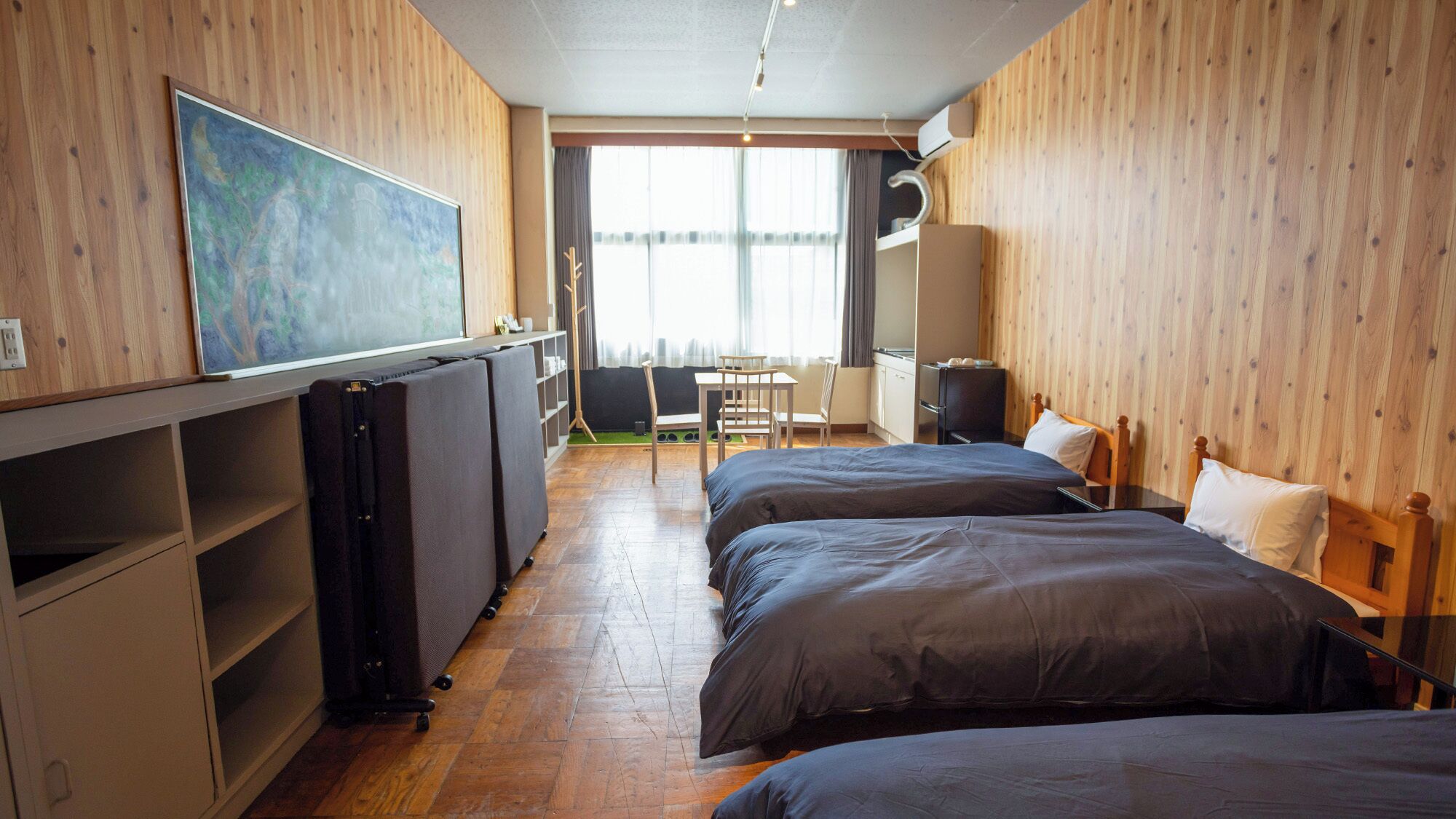 A hotel room with two beds, a desk, a chair, a radiator, and a painting on the wall.