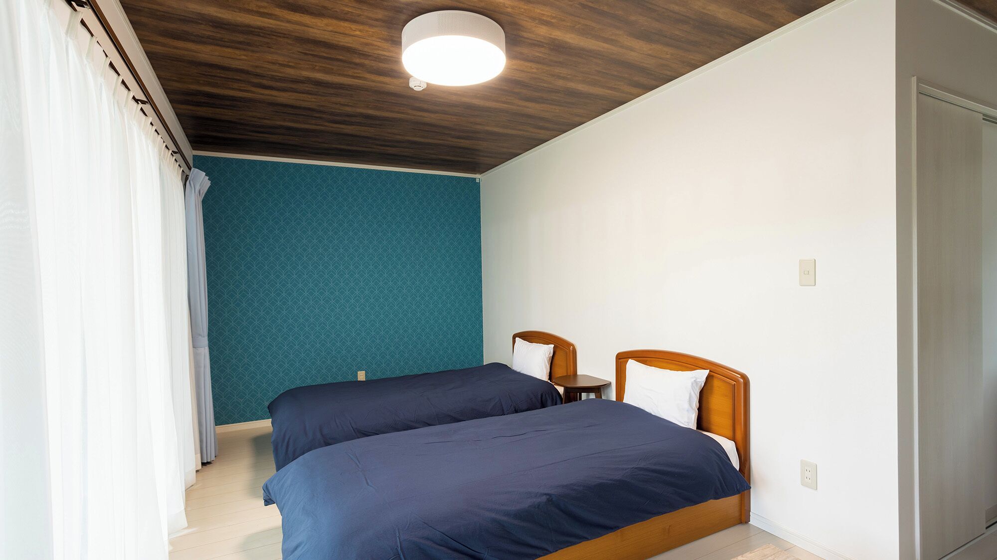 A bedroom with two beds, a wooden ceiling, and a teal wall.