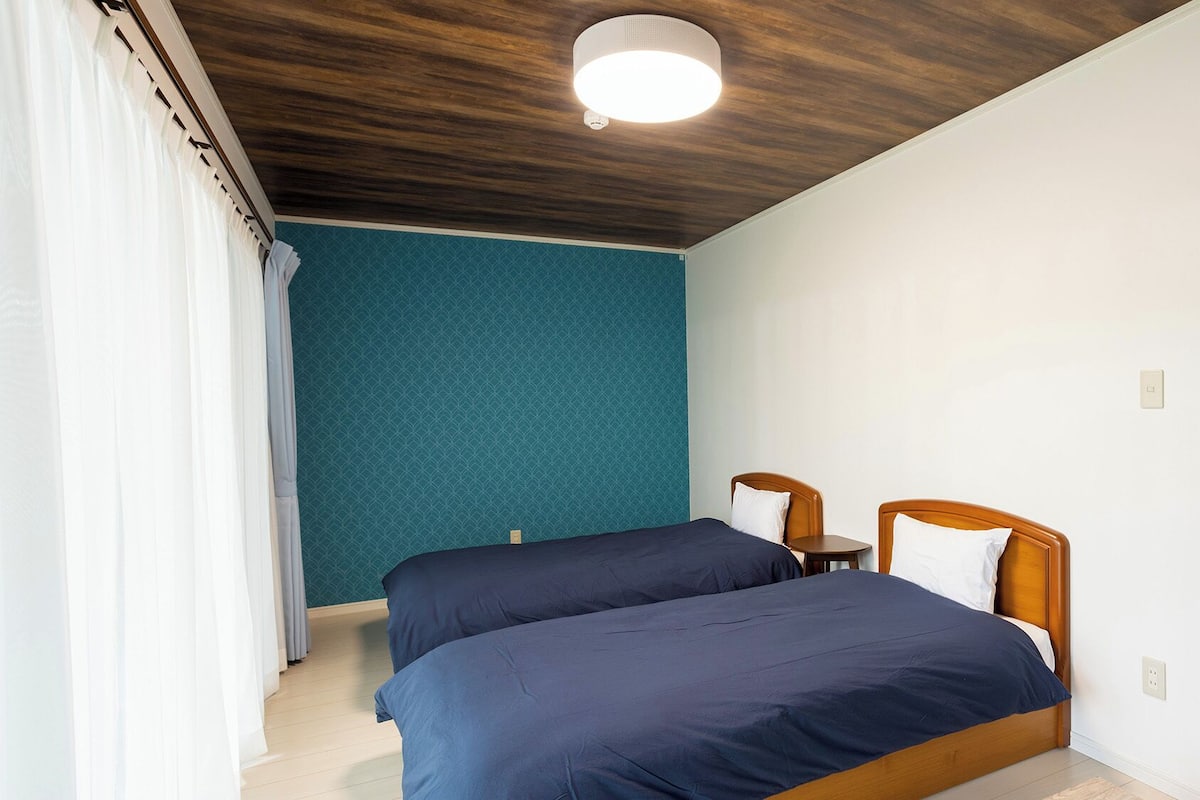 A bedroom with two beds, a wooden ceiling, and a teal wall.
