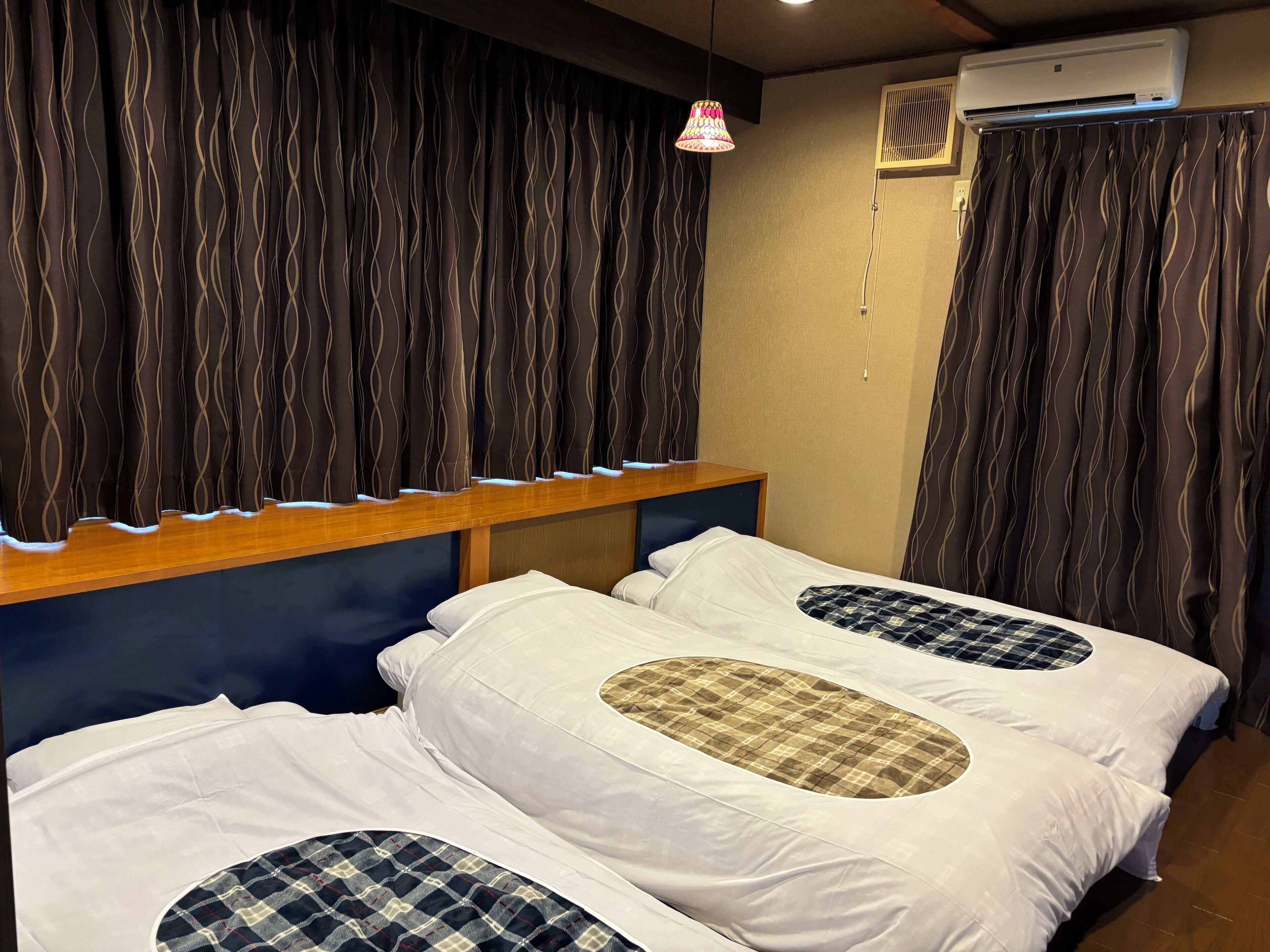 A room with two beds, a wooden headboard, an air conditioning unit, and a hanging lamp.