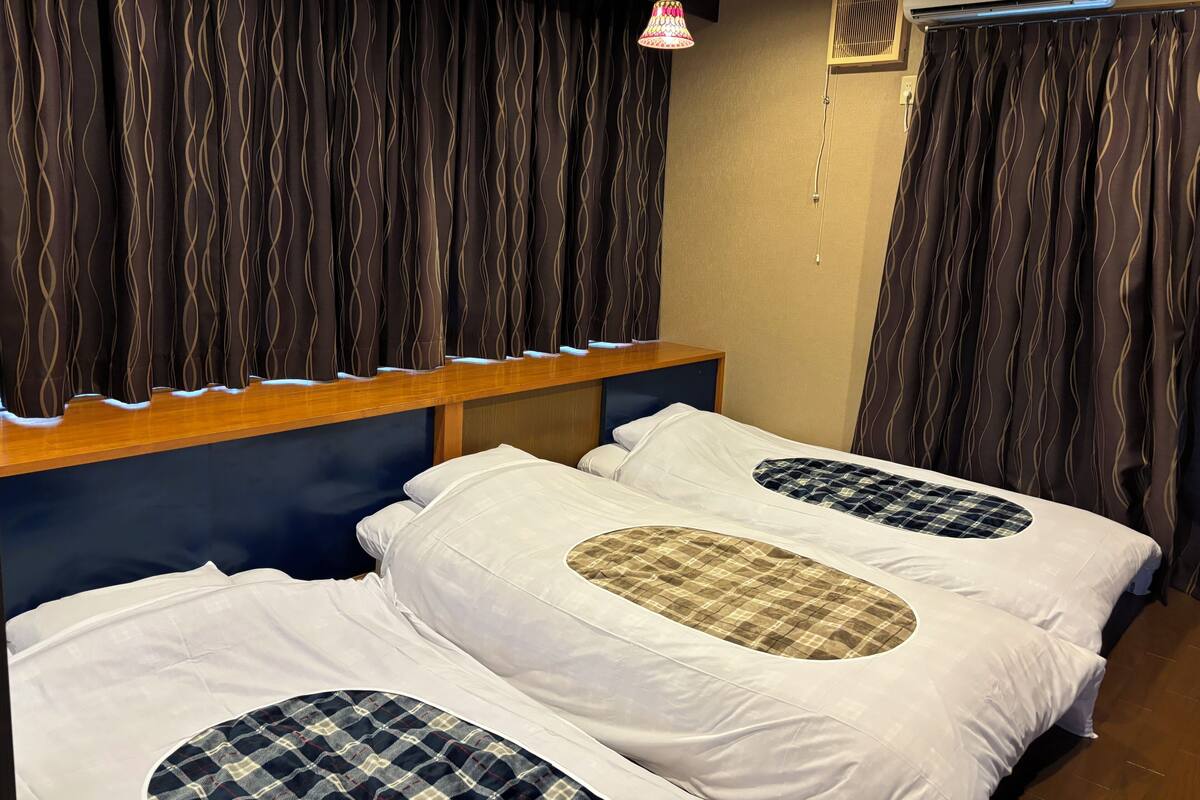 A room with two beds, a wooden headboard, an air conditioning unit, and a hanging lamp.