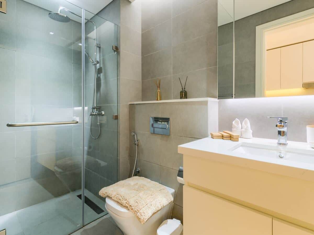 Une salle de bain moderne avec une douche à parois de verre, des toilettes agrémentées d’une serviette beige, et un meuble-lavabo blanc avec un miroir et un évier.