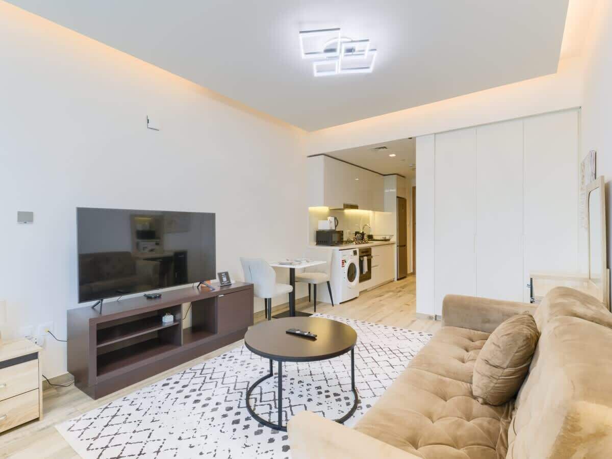 A modern living room with a flat-screen TV, a sofa, a coffee table, and a kitchen area in the background.