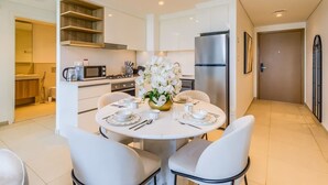 Una cucina moderna con mobili bianchi, un frigorifero in acciaio inossidabile e un'area pranzo con un tavolo bianco apparecchiato per quattro persone.