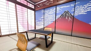 Tatami-mattoilla päällystetty huone, jossa on matala pöytä ja tuoli, shoji-paperi-seinä, jossa on vuoristomaisema, ja suuri ikkuna, josta avautuu näkymä ulos.