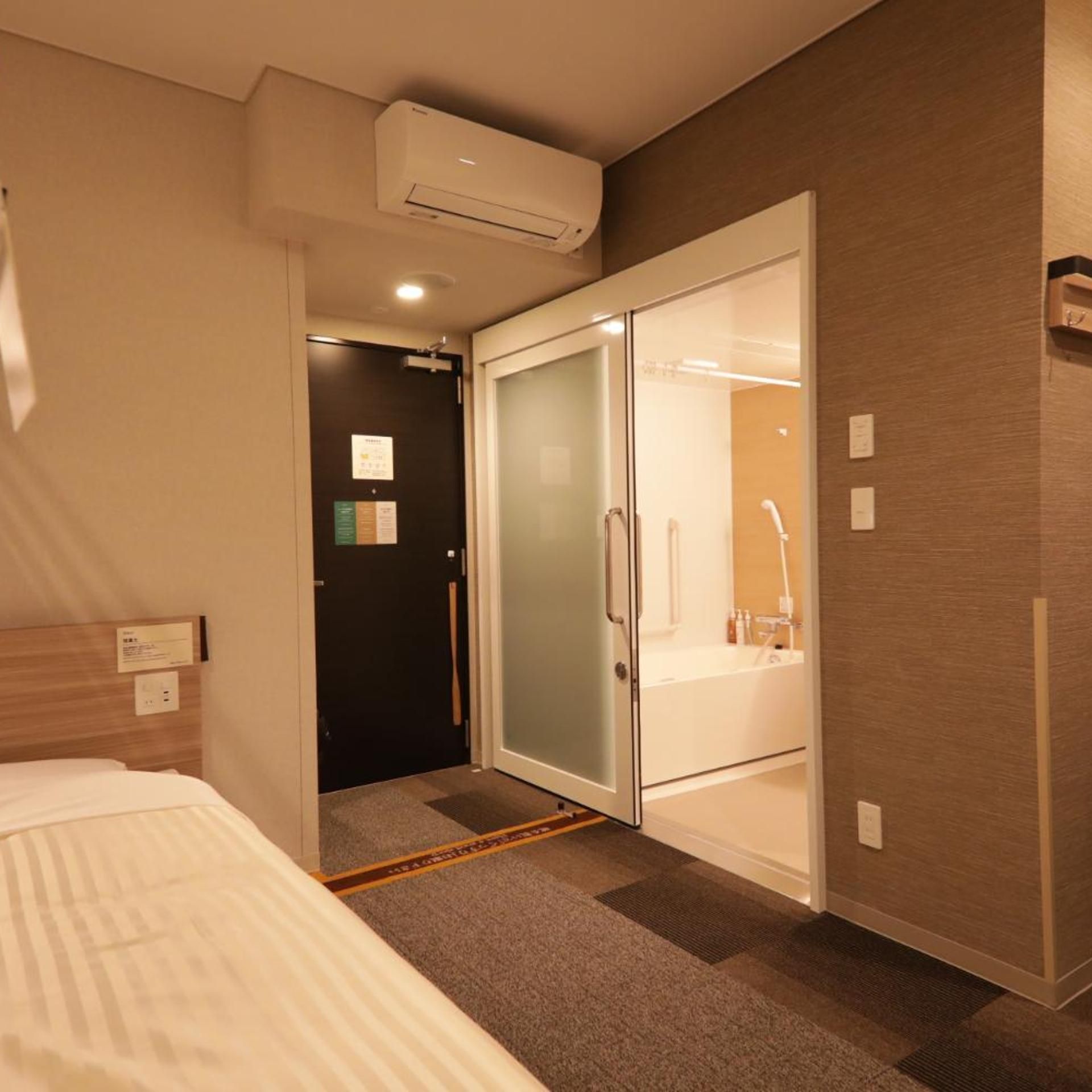 A hotel room with a bed, a wardrobe with a mirror, and a shower area.