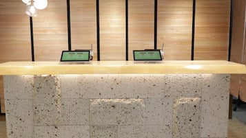 A reception desk with two laptops, wooden paneling on the wall, and pendant lighting.