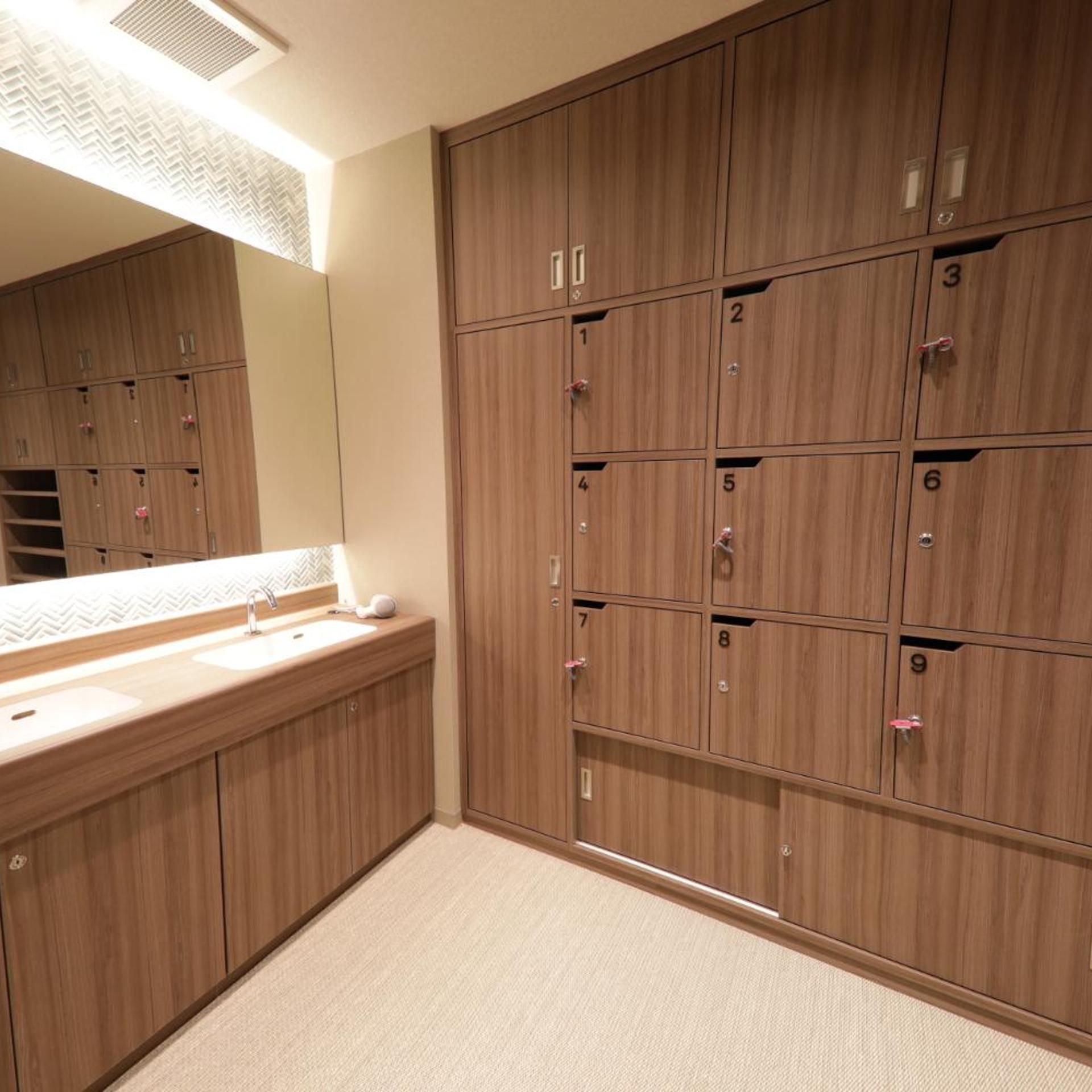 A hotel bathroom with wooden lockers, a sink, and a mirror.