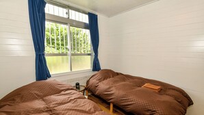 Una habitación con dos camas, una ventana con cortinas azules y una mesita con una tetera.
