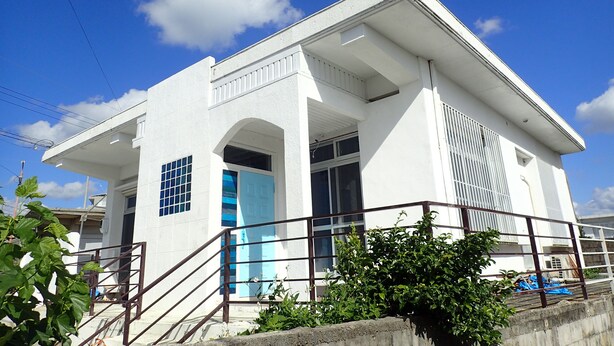 Un edificio blanco con puerta azul, una escalera y barandilla metálica.