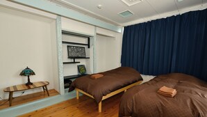 Un dormitorio con dos camas, una mesita, una lámpara y una estantería con objetos decorativos.