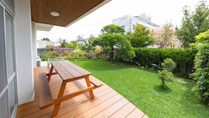 A wooden deck with a picnic table, a grassy backyard, and a variety of plants and trees.