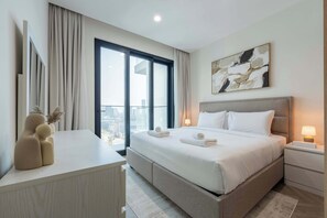 A modern hotel room with a large bed, a desk, and a view of the city. - Brand New, Luxury Furnished 1BR, Prime Location (Dubai)