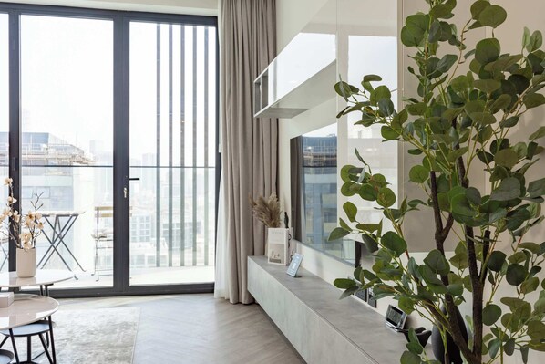 A modern living room with a large sliding glass door leading to a balcony, a potted plant, and a minimalist design. - Brand New, Luxury Furnished 1BR, Prime Location (Dubai)