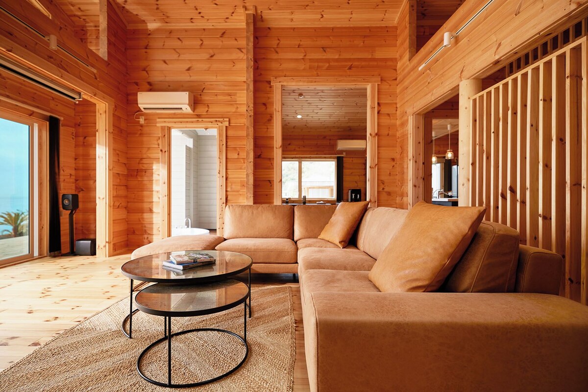 Un intérieur en bois avec un canapé, une table ronde et une vue à travers une porte vitrée.