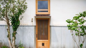 Una puerta de madera con listones verticales, un pequeño ventanal encima y un timbre de pared.