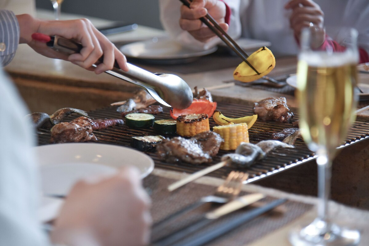 A dining table with various grilled meats, vegetables, and a glass of champagne.