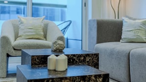 Ein modernes Wohnzimmer mit einem grauen Sofa, einem grauen Sessel und einem schwarzen Marmor-Couchtisch mit zwei weißen Kerzen.