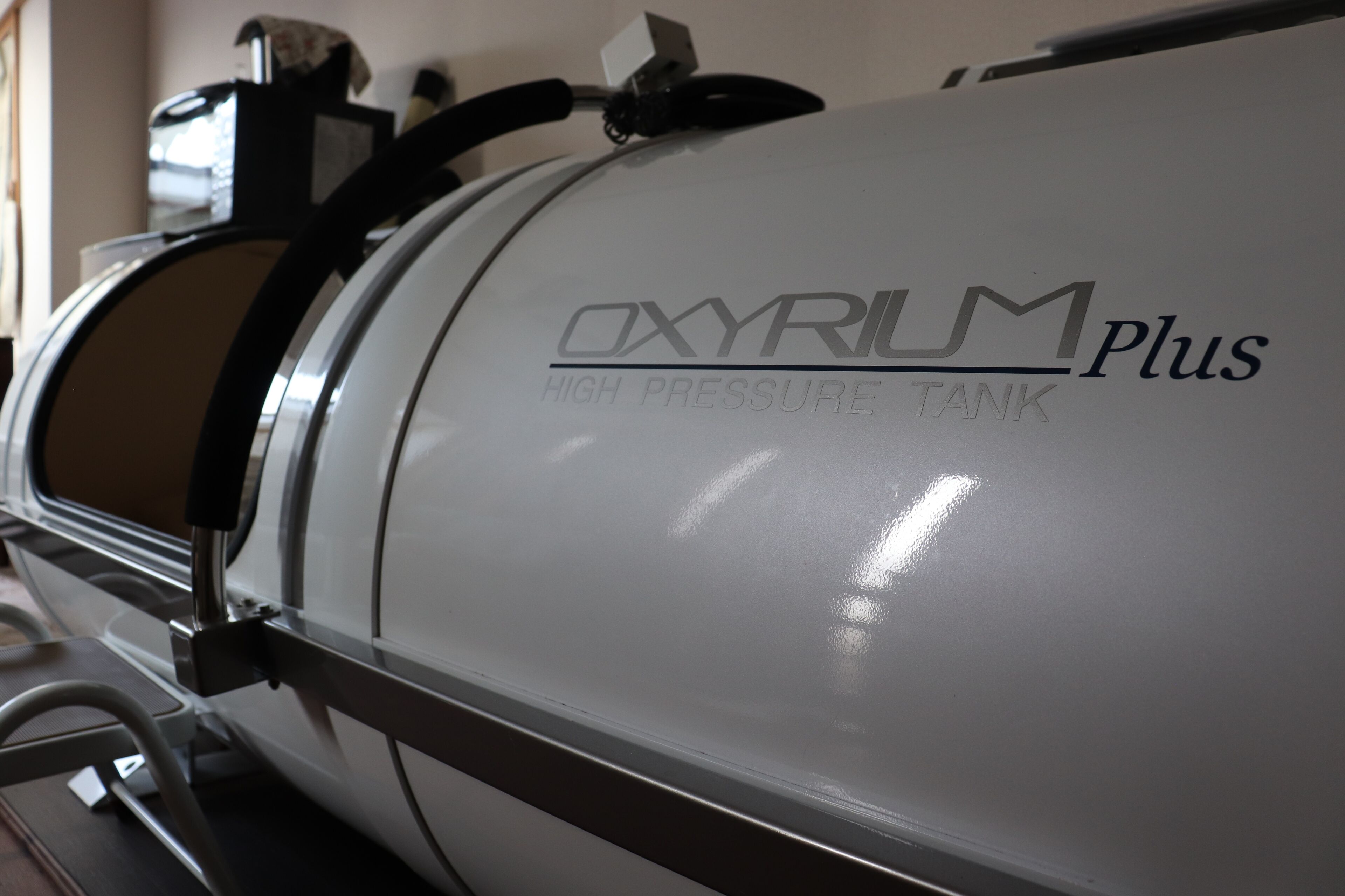 A white oxygen tank labeled "OXYRUM Plus High Pressure Tank" with a metallic frame.