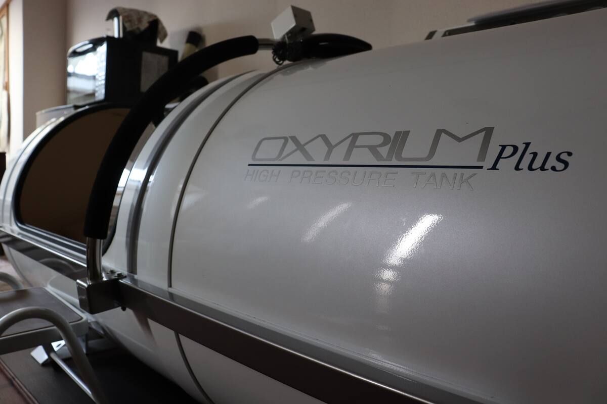 Um cilindro de oxigênio branco com a etiqueta "OXYRUM Plus High Pressure Tank" e uma estrutura metálica.