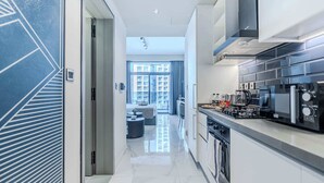 Una cocina moderna con una isla central, un área de comedor con sofá y mesa, y vista a un edificio residencial a través de grandes ventanales.