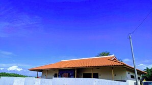 A single-story building with a red-tiled roof, a concrete wall in the foreground, and a clear blue sky. - B/C Hotel Naha Rent-a-car Hotel (Ishigaki)
