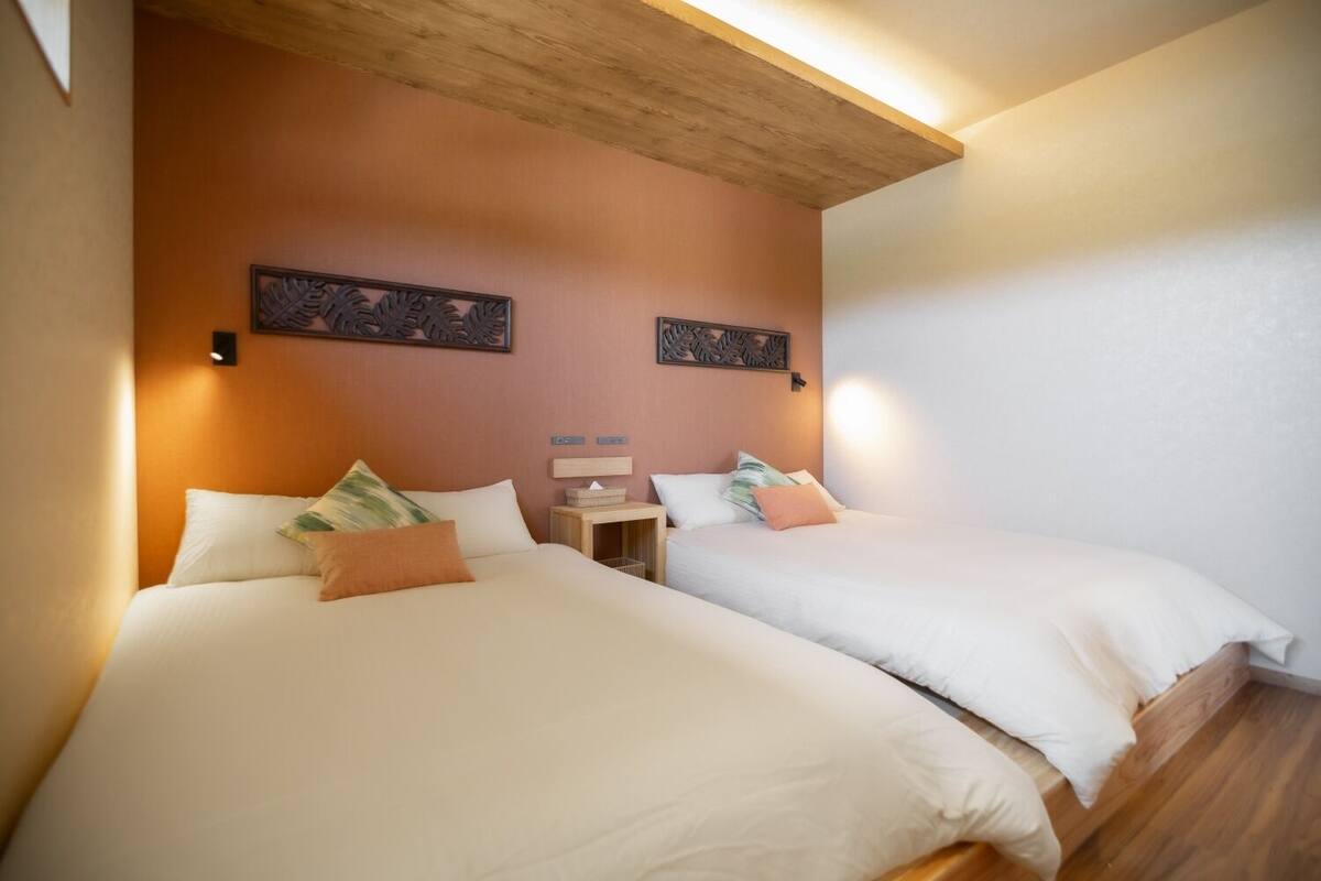 A hotel room with two beds, wooden headboard, wall art, bedside tables, and a ceiling light.