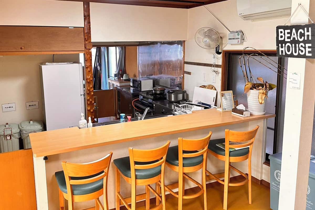 A compact kitchen with a wooden bar, four wooden chairs, a sink, and a refrigerator.