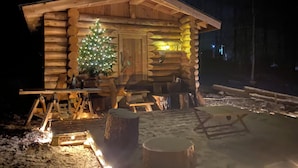 En hytte med en juletræ, bålsted og en bænk udenfor.