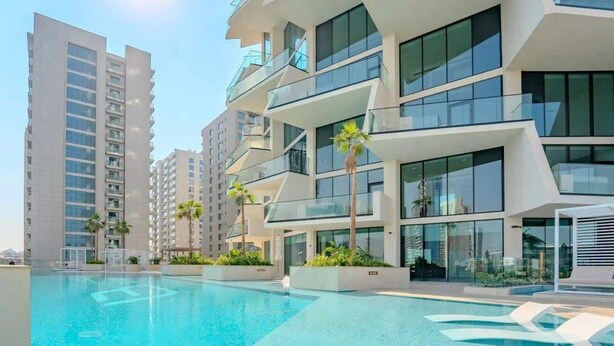 Un immeuble résidentiel moderne doté d’une piscine, de balcons et offrant une vue sur un ciel dégagé.