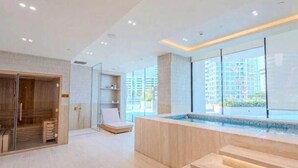 Un espace spa moderne comprenant un sauna en bois, un salon de détente et une grande fenêtre offrant une vue sur la ville.