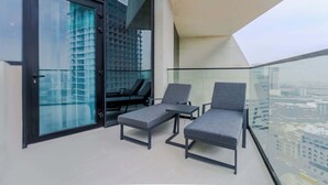 Un balcon avec deux fauteuils de jardin gris, une porte vitrée et une vue sur la ville.