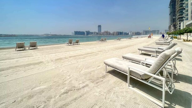 Un espace de détente aménagé au bord de la plage, avec des chaises longues et une vue sur la mer et le paysage urbain.